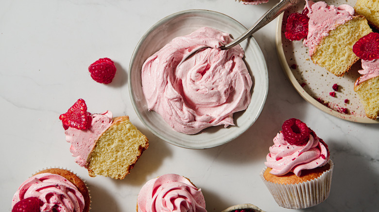 Pink whipped cream in a bowl and iced onto cupcakes