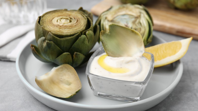 Cooked artichokes with a leaf being dipped in sauce