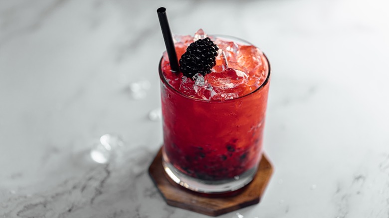 Red cocktail garnished with blackberry on marble surface