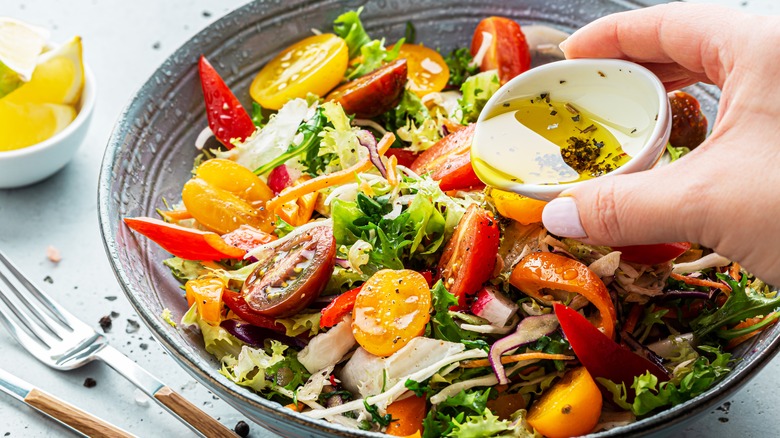 Hand pouring dressing on salad