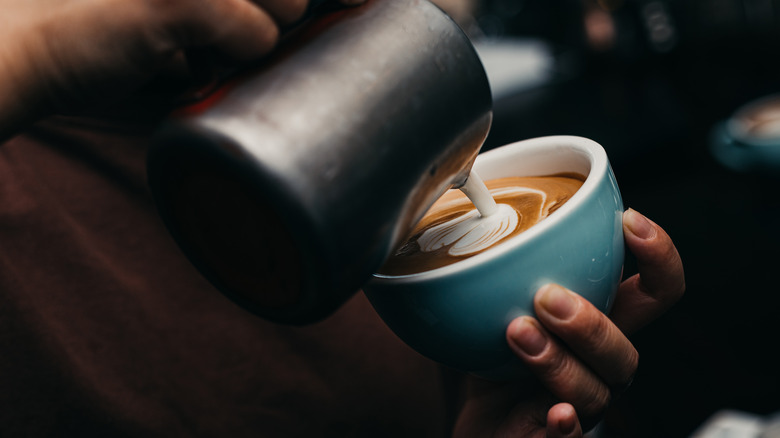 Barista pouring frothy milk into coffee