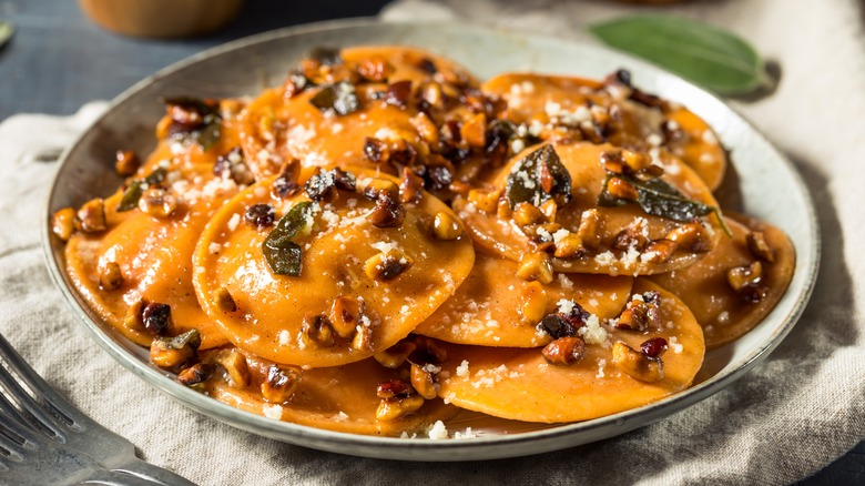 butternut squash ravioli with sage and hazelnuts on round dinner plate atop kitchen towel