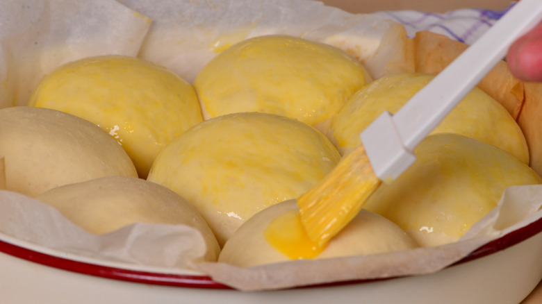 rolls in a baking dish being brushed with egg wash