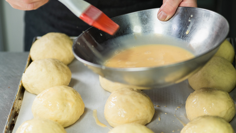 holding bowl filled with egg wash over tray or rolls