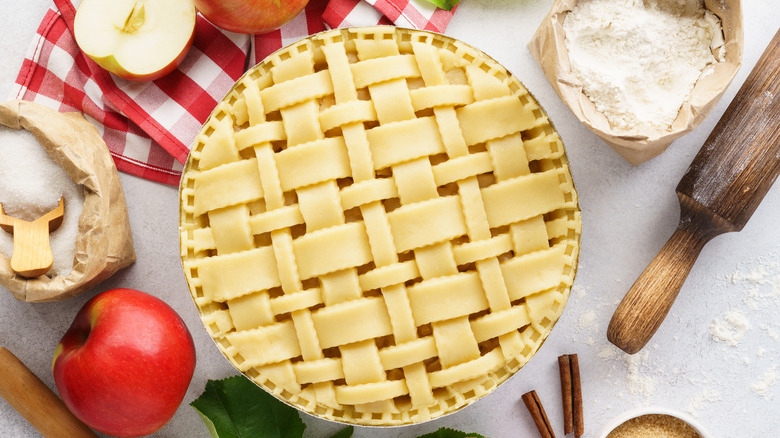 Overview of unbaked lattice-top apple pie surrounded by apples and baking ingredients