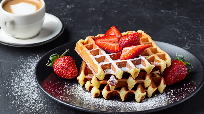 homemade cake batter waffles on a plate with a cappuccino on a dark background