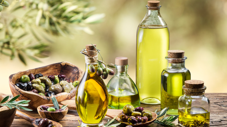 Clear glass bottles of olive oil on a wooden table with olive fruit