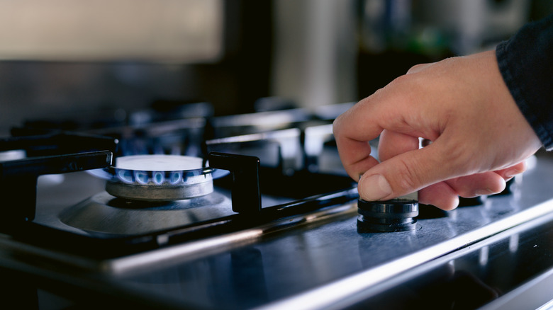 hand turning on stove burner