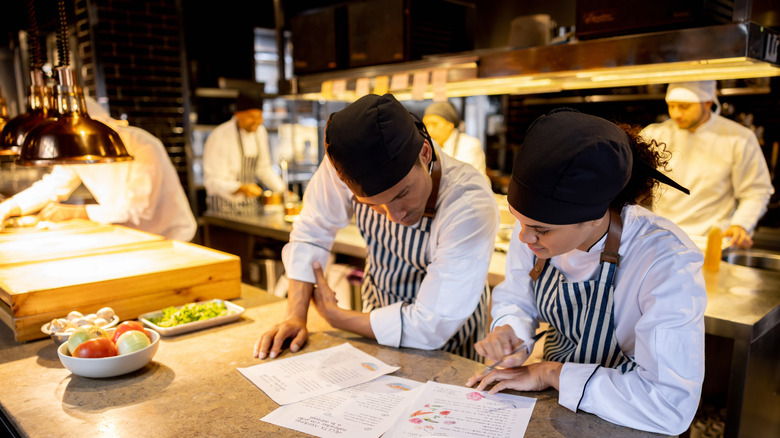 cooks in restaurant looking at recipes in kitchen