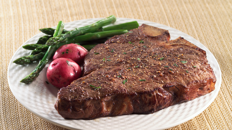 t-bone on white plate with red potatoes and asparagus