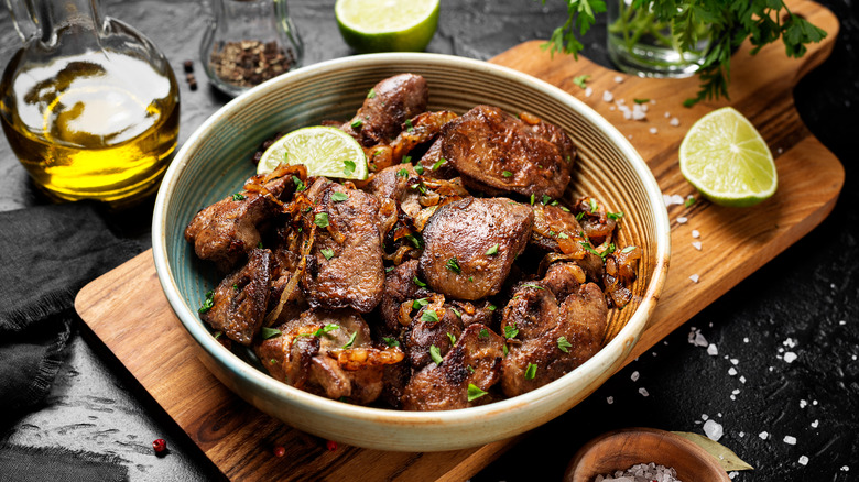 A bowl of cooked liver and onions on a wooden plate.