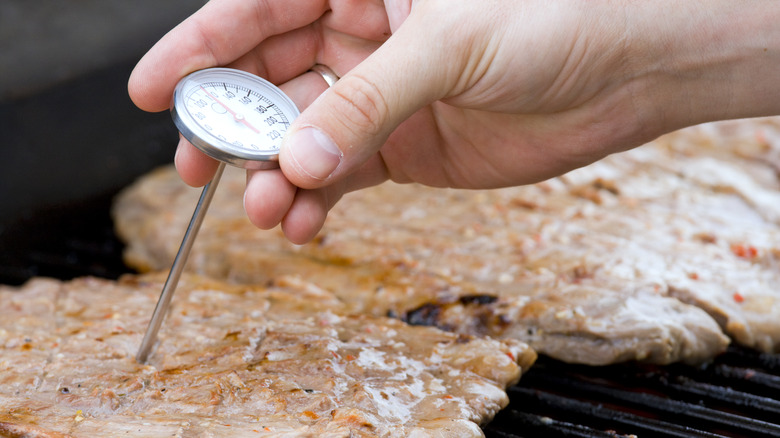 Hand putting meat thermometer into beef