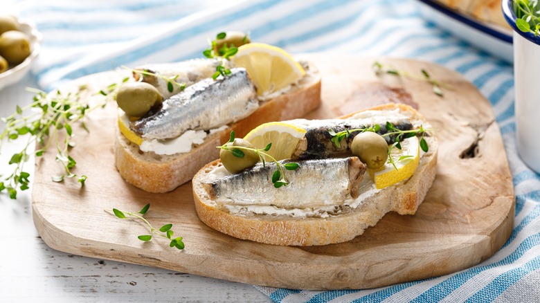 Canned sardines on buttered sliced bread, with olives, lemon slices, and greens