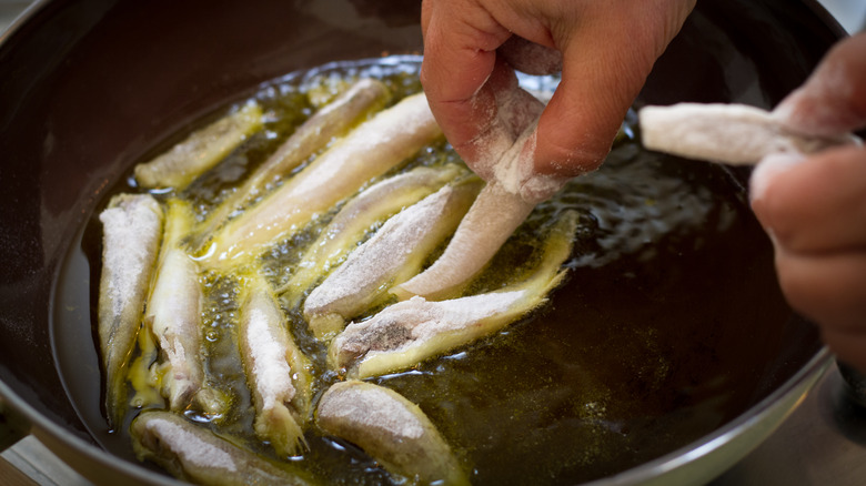 person placing flour-coated sardines in pan to fry