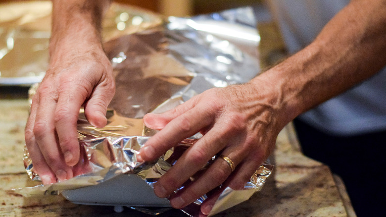 person covering casserole dish with foil