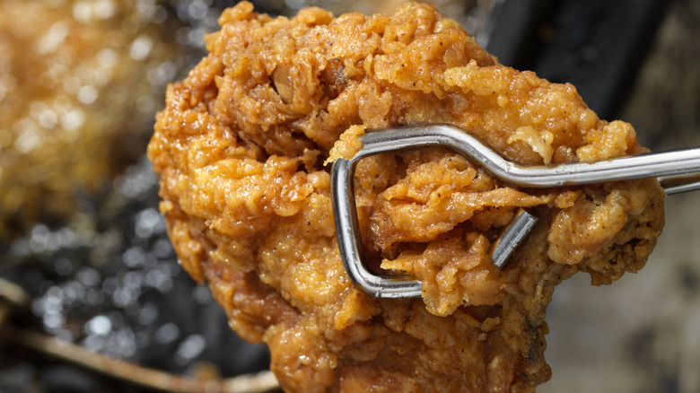 Tongs holding fried chicken