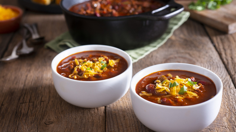 two bowls of homemade chili with a pot in the background and cornbread