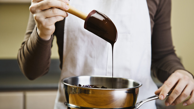 woman in apron stirring pot of melted chocolate with a spatula