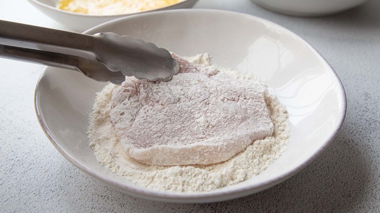 tongs holding a floured pork chop