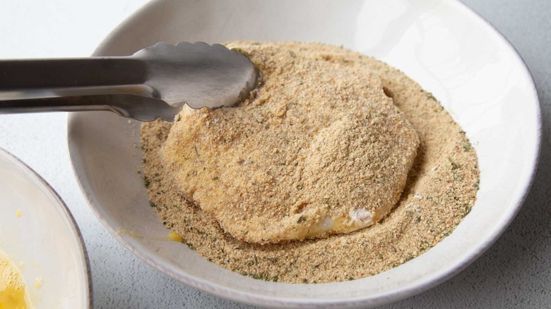 tongs holding a pork chop in breadcrumbs