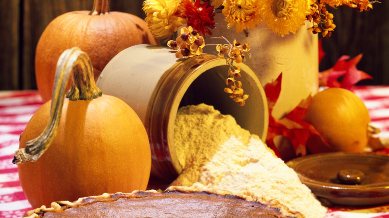 Sugar pumpkins on a table with a jar of flour, flowers, and a pumpkin pie