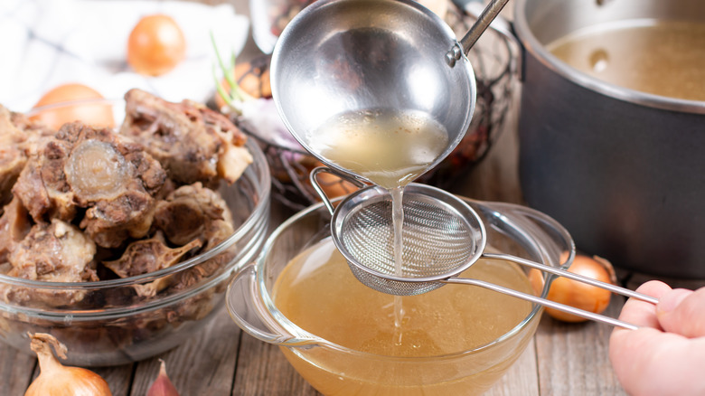 Person straining bone broth into bowl