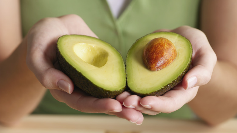 A woman holds two halves of an avocado