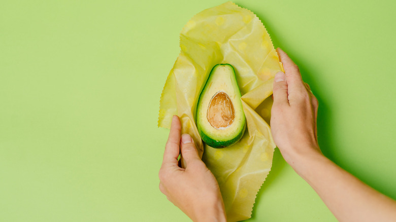 A person wraps an avocado in wax paper