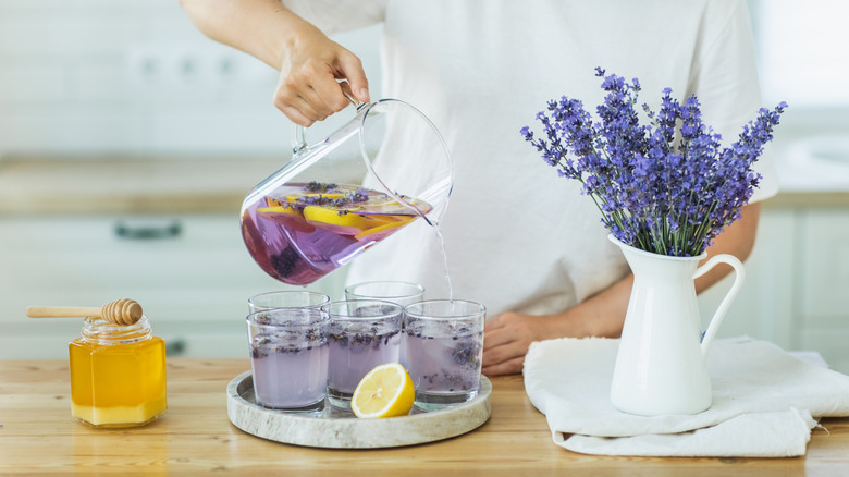 Person pouring purple lemonade alongside lavender bouquet