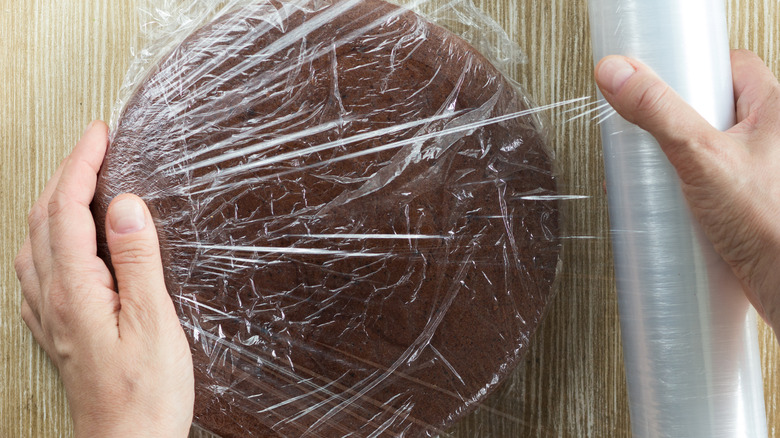 wrapping chocolate cake in plastic wrap on cutting board