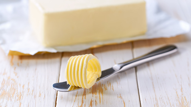 Curl of butter on knife with unfocused stick of butter in background