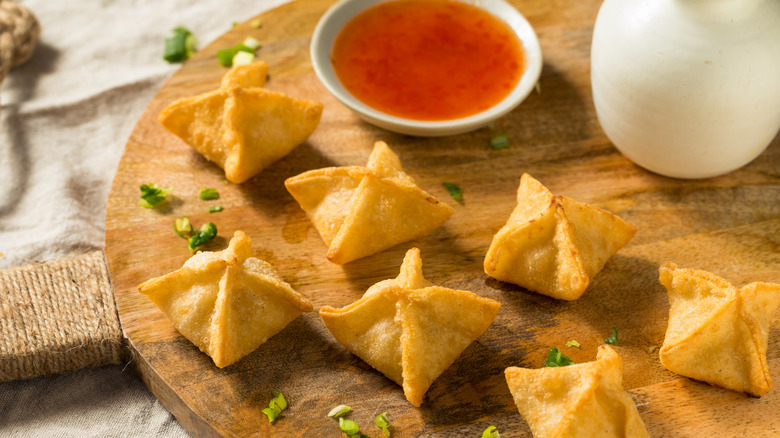 crab rangoon on wooden cutting board next to dish of sweet chile sauce