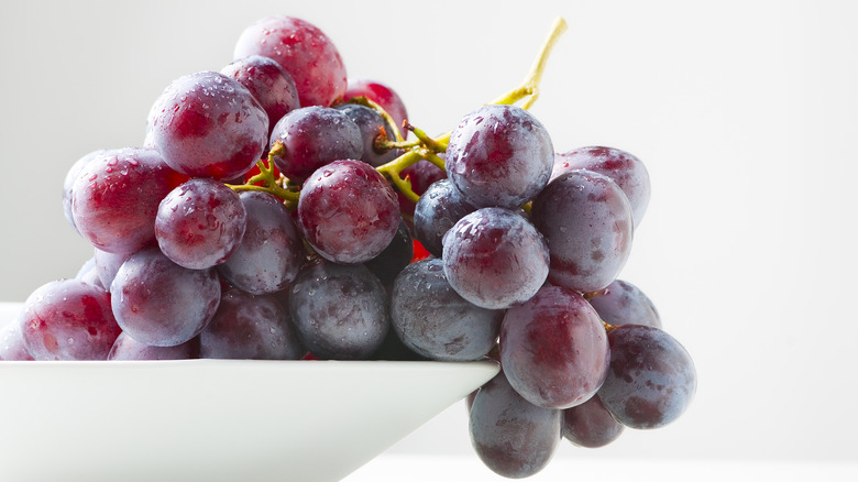 a bunch of red grapes spilling out of white bowl