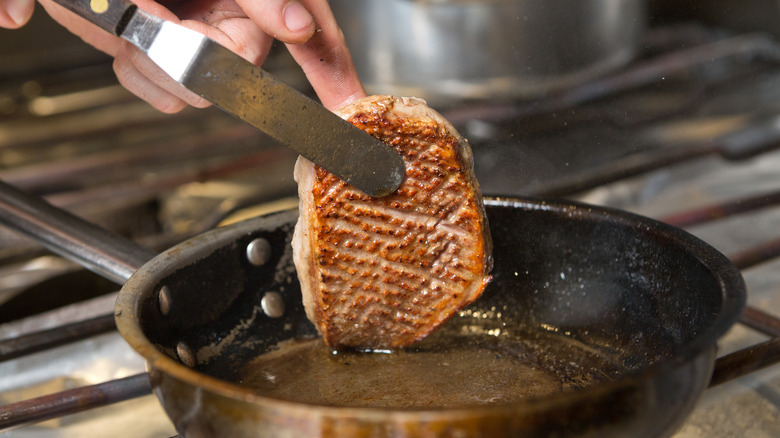 A scored duck breast searing in a pan