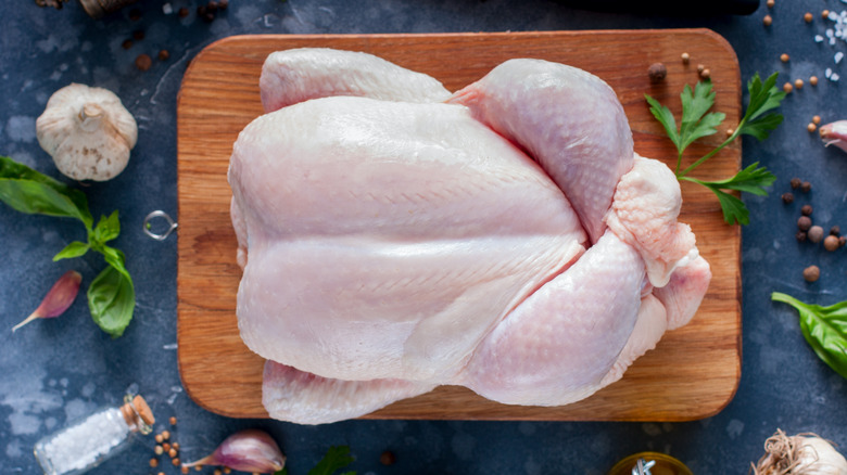 whole raw chicken on wooden board