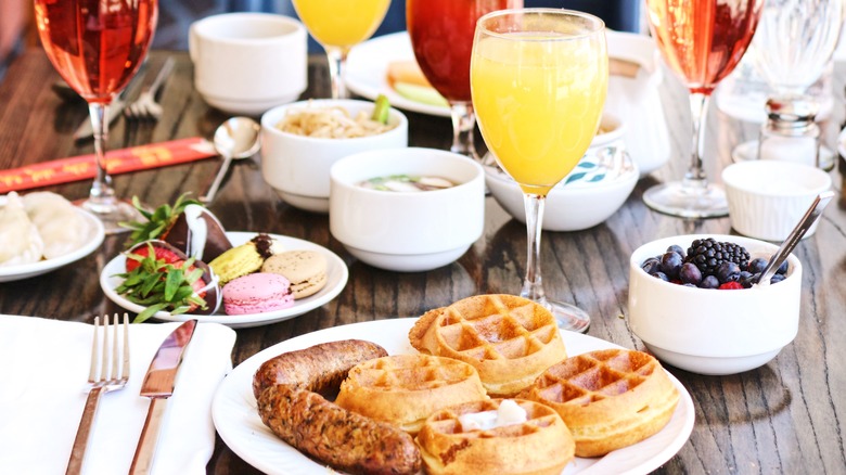 Brunch table with drinks, waffles, sausage, and fruit