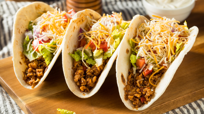 three soft shell ground beef tacos topped with shredded cheese