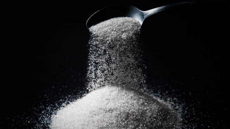 Spoon pouring sugar black background