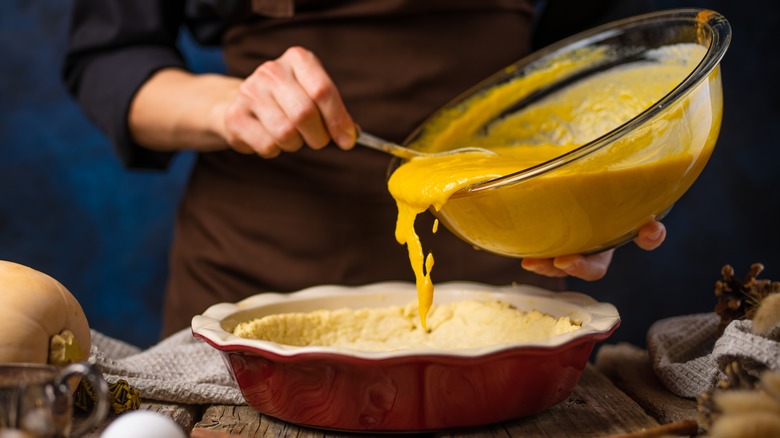 Person pouring pie filling into crust