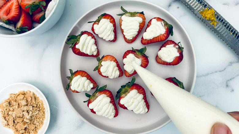 piping cheesecake mixture into strawberries