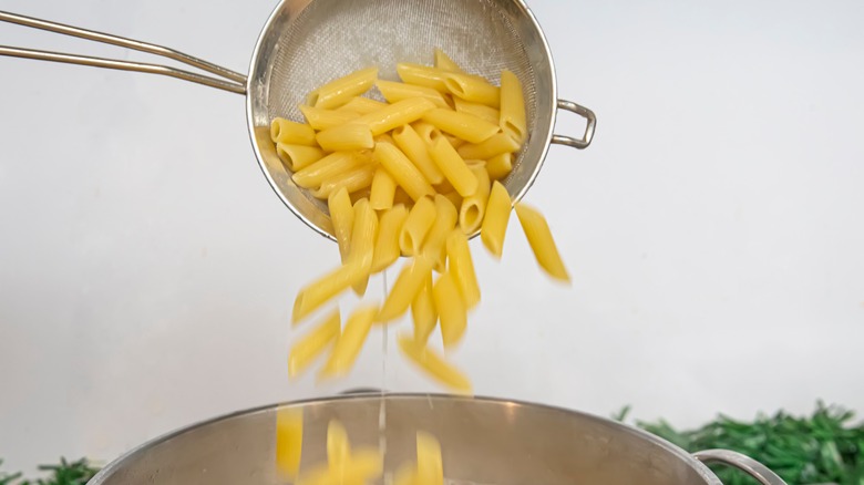 Penne pasta being poured into a pot