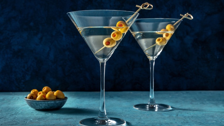 Two martinis with olives next to a bowl of olives