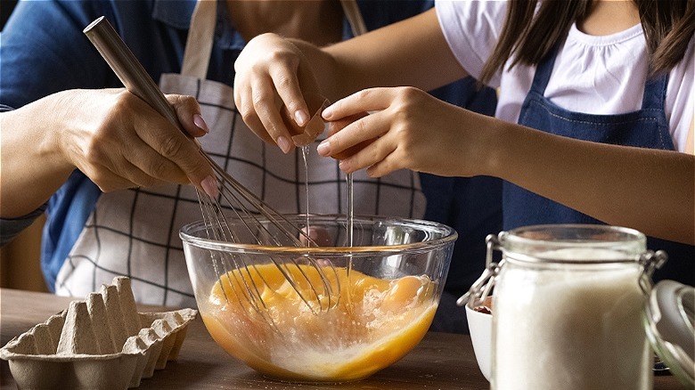 Hands adding egg to mixing bowl