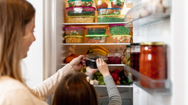 a woman and her daughter grab an item from a refrigerator