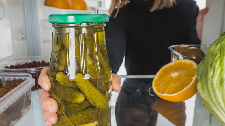 Woman grabbing jar of pickles from fridge 