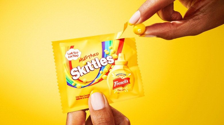 Hands holding a mustard-flavored Skittles pack