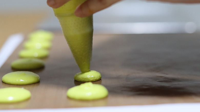 piping macarons onto baking sheet