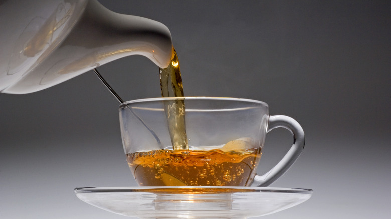 Tea pouring from teapot into clear glass teacup