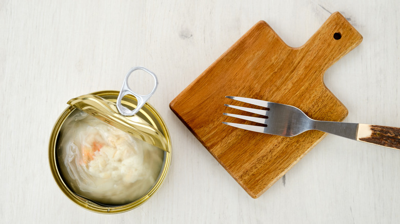 canned crab next to fork and wooden board