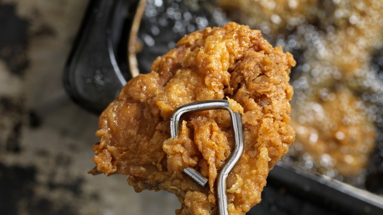 Fried chicken held by tongs over deep fryer